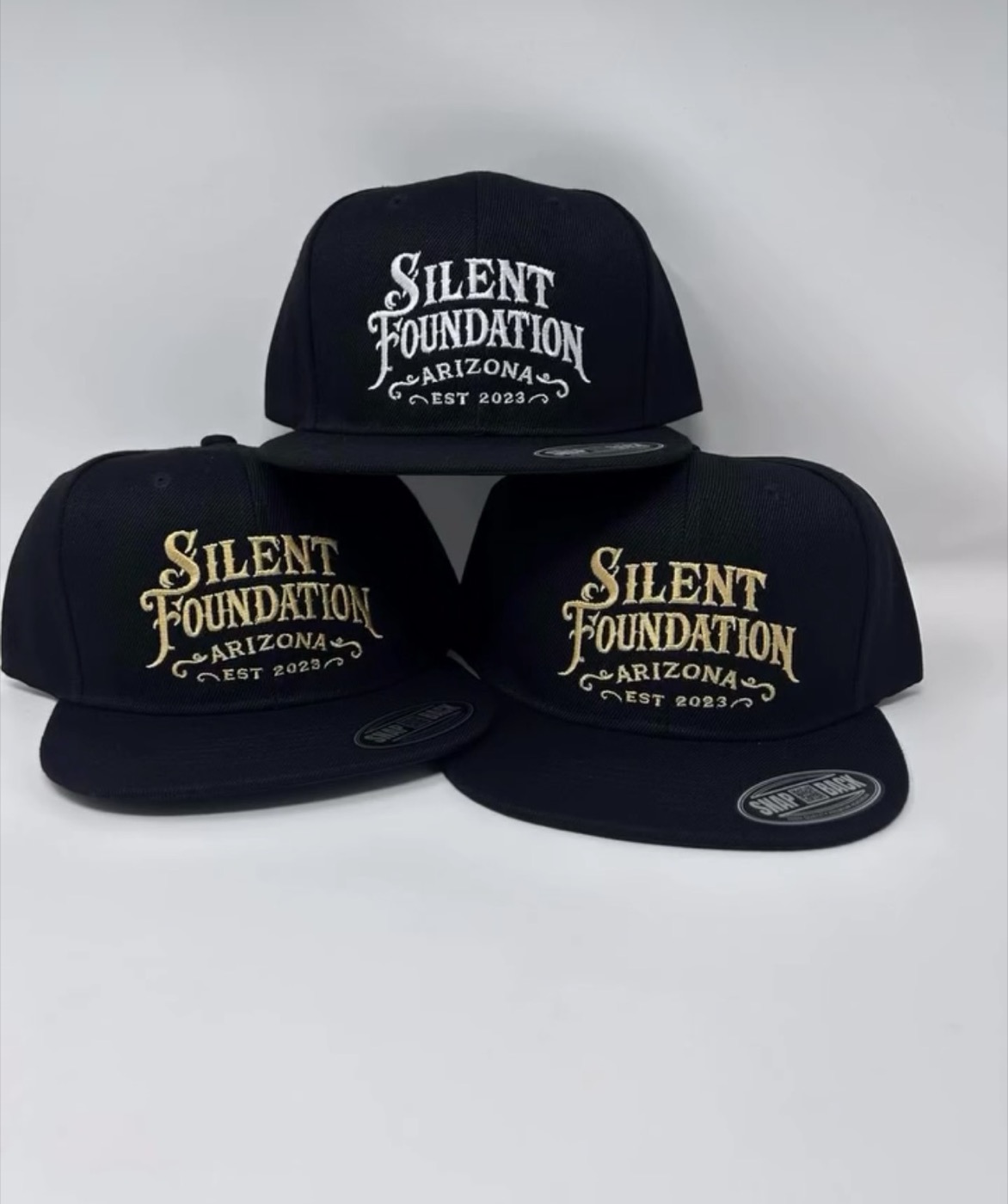 Three black snapbacks with Silent Foundation Arizona embroidered in white and gold