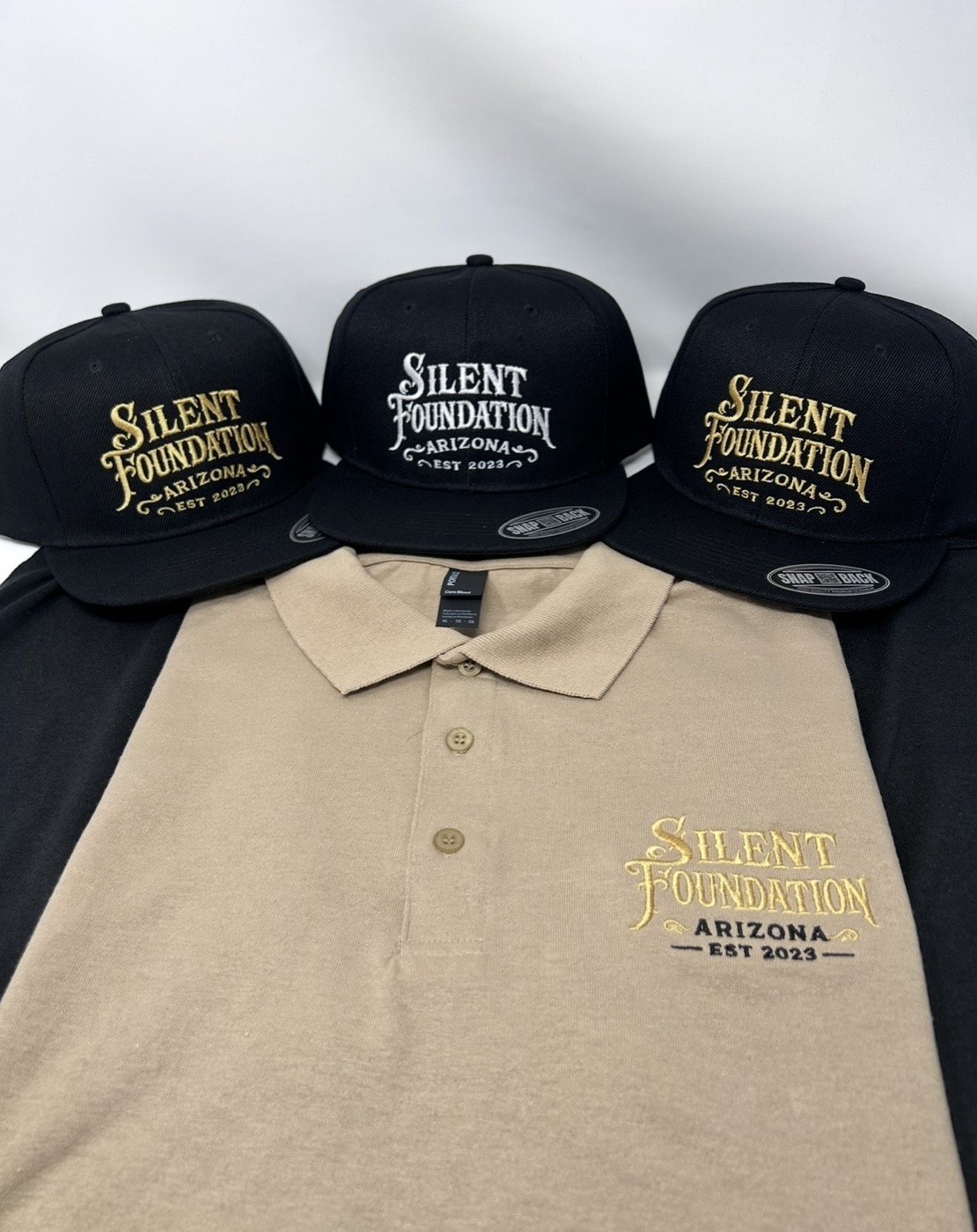 Silent Foundation snapbacks and a tan polo laid out as a matching uniform kit